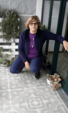 a woman wearing glasses and a purple shirt is squatting down