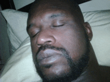 a man with a beard is sleeping in bed with his eyes closed