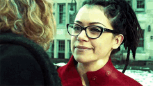 a woman with dreadlocks wearing glasses and a red jacket is looking at another woman .