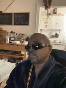 a man wearing sunglasses sits in front of a chalkboard that says move car tues-weds