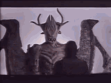 a man is standing in front of a statue of a demon with horns .