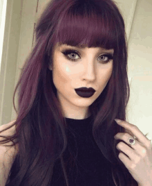 a woman with purple hair and black lipstick is wearing a ring on her finger