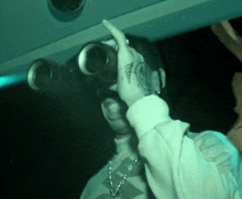 a man with a tattoo on his hand is looking through binoculars in a dark room .