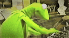 kermit the frog is sitting at a table looking at a keyboard .