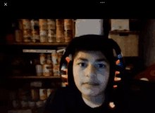 a boy wearing headphones looks at the camera in front of a shelf of cans