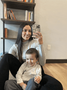 a woman is taking a selfie with a baby in front of a bookshelf