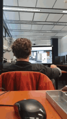 a man sits at a desk in front of a computer monitor with a mouse on the desk in front of him