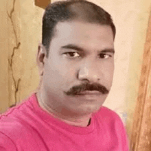 a man with a mustache is wearing a pink shirt and looking at the camera .