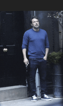 a man in a blue sweater is smoking a cigarette in front of a black door