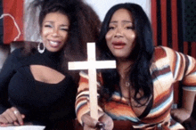 two women standing next to each other holding a wooden cross