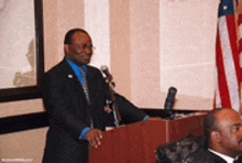 a man in a suit and tie is standing at a podium with microphones