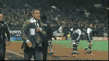 a man in a suit and tie stands on a soccer field in front of a sign that says portland