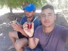 a man wearing a blue cap with the word boca on it sits next to another man