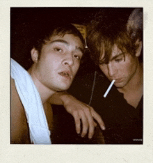 a man smoking a cigarette next to another man without a shirt on