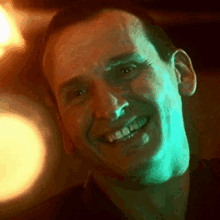 a close up of a man 's face smiling with a green light behind him