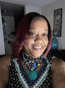 a woman with red hair is smiling and wearing a necklace with a green pendant