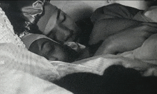 a black and white photo of a man and a woman sleeping in a bed