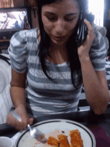 a woman in a striped shirt is talking on a cell phone while sitting at a table with a plate of food