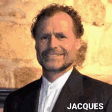 a man with curly hair and a beard is wearing a black suit and white shirt with the name jacques on the bottom