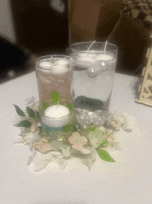 two candles in a glass with water and pearls on a table