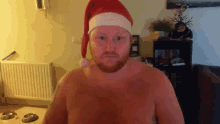 a shirtless man wearing a santa hat stands in a living room