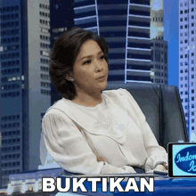 a woman is sitting in front of a screen that says ' buktikan ' on it