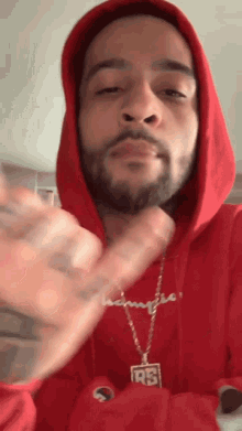 a man with a beard wearing a red hoodie and a gold chain .