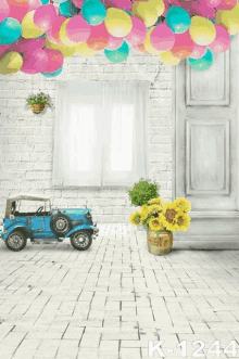 a blue toy car sits in a room with balloons hanging from the ceiling and sunflowers in a vase