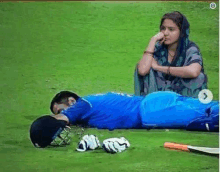 a woman is sitting next to a cricket player who is laying on the grass .