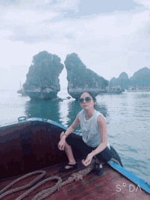 a woman sits on the side of a boat in the water with a rock in the background