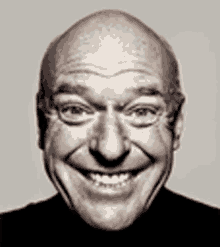 a bald man with glasses is smiling in a black shirt .