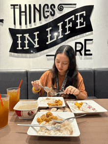 a girl sits at a table with plates of food and a sign that says things in life