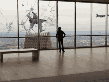 a man stands in front of a broken window with a picture of a plane flying through it