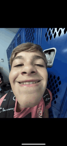 a boy wearing a champion backpack is smiling in front of a blue locker