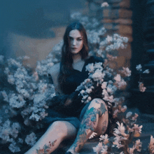 a woman with tattoos on her legs is sitting in a field of flowers