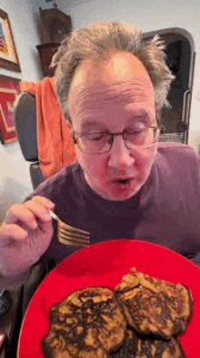 a man in a wheelchair is eating pancakes with a fork from a red plate .