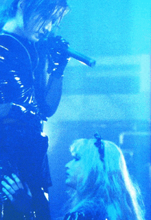 a man singing into a microphone next to a woman with blonde hair