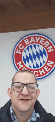 a man wearing glasses stands in front of a sign that says fc bayern munich