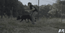 a man is running with a black dog in front of a chain link fence with the letters a & e visible