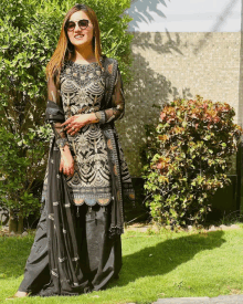 a woman wearing a black dress and sunglasses stands in the grass