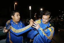 a man wearing a blue and yellow adidas shirt talks to another man