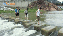 three men are crossing a river on a set of stepping stones with a sign in the background that says ' 2 '