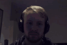 a man wearing headphones looks at the camera with a dark background