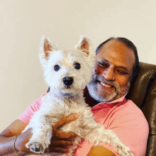 a man in a pink shirt holds a small white dog in his arms