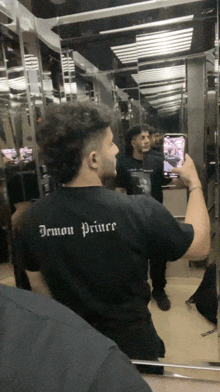 a man taking a picture of himself in an elevator with a shirt that says demon priver on the back