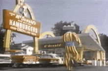 a man in a striped suit is walking in front of a mcdonald 's hamburgers sign .