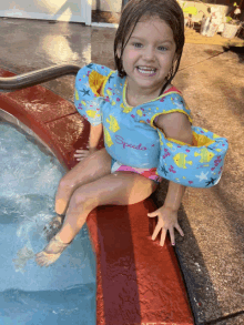 a little girl wearing a speedo life preserver is sitting in a pool