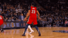 a basketball player wearing a red jersey with the number 23 on it is dribbling the ball on a basketball court .