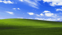 a grassy hill with a blue sky and clouds in the background