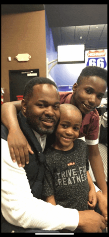 a man and two children are posing for a picture and one of the children is wearing a shirt that says " strive for greatness "